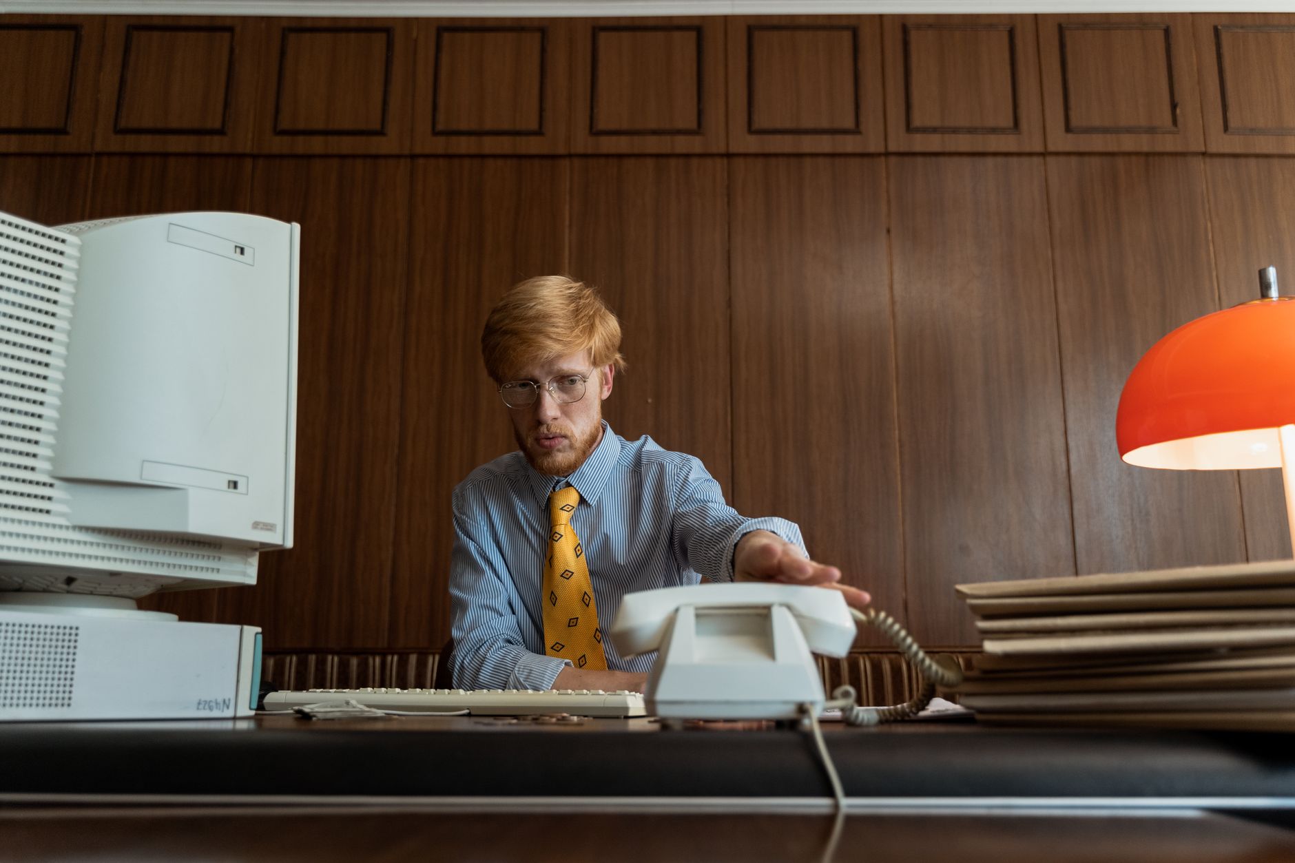 Employé de bureau tendant la main vers un téléphone fixe d'époque, décor années 70